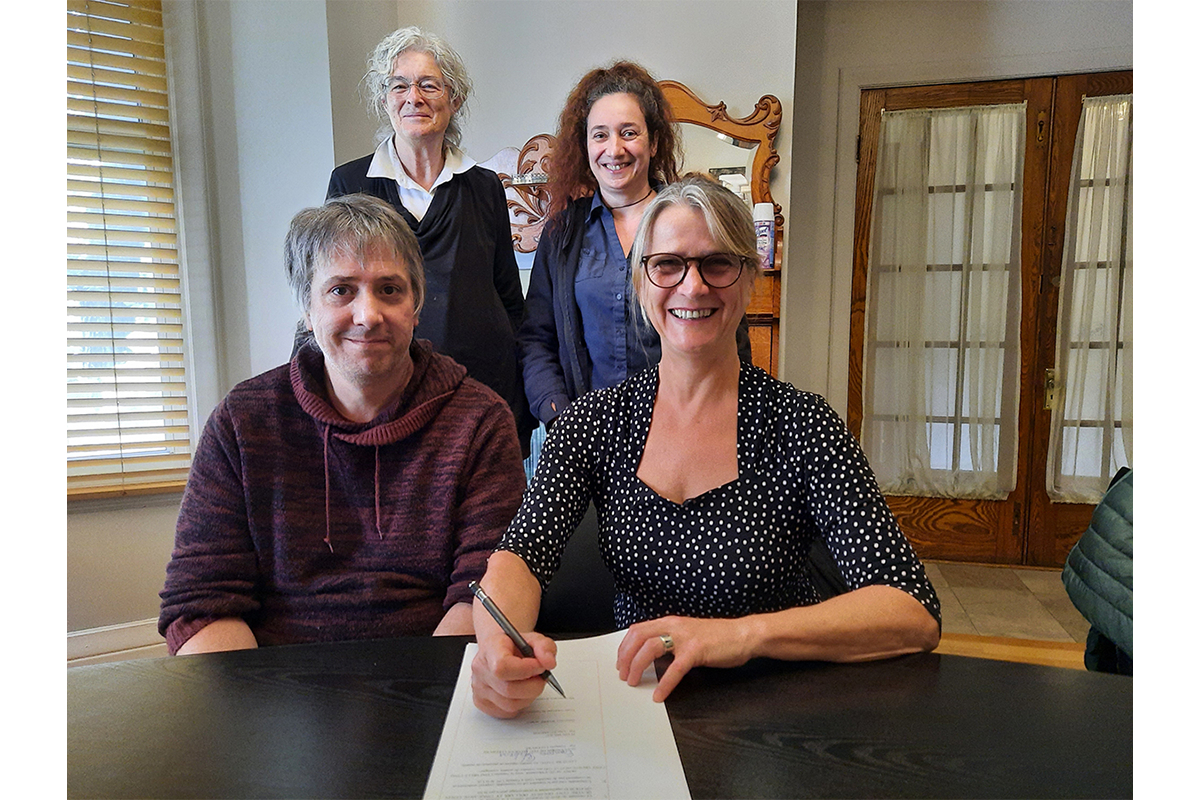 Line St. Amour, executive director of Plein Milieu, signs ownership papers for the organization’s newly purchased building while seated next to François Lefebvre, who’s father owned said property for many years. Board members Isabelle Raffestin (right) and Linda Roy (left) look on.