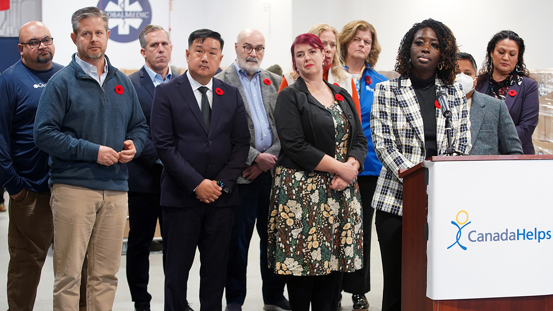 Alice Wiafe, President, Black Mental Health Canada, takes a question at the podium, backed by, left to right: Rahul Singh, Executive Director, GlobalMedic; Neil Hetherington, CEO, Daily Bread Food Bank; Richard Matern, Director of Research, Food Banks Canada; Duke Chang, President and CEO, CanadaHelps; Bill Harper, Vice President, Imagine Canada; Suzanne Duncan, Vice President, Philanthropy, Canadian Women’s Foundation; Marie MacCormack, Vice President, Philanthropy and Communications, Fred Victor; Julia Deans, President and CEO, Habitat for Humanity Canada; Lauren Pragg, Interim Executive Director, Lesbian Gay Bi Trans Youth Line; and Audrey Rochette, Executive Director, Anishnawbe Health Foundation.