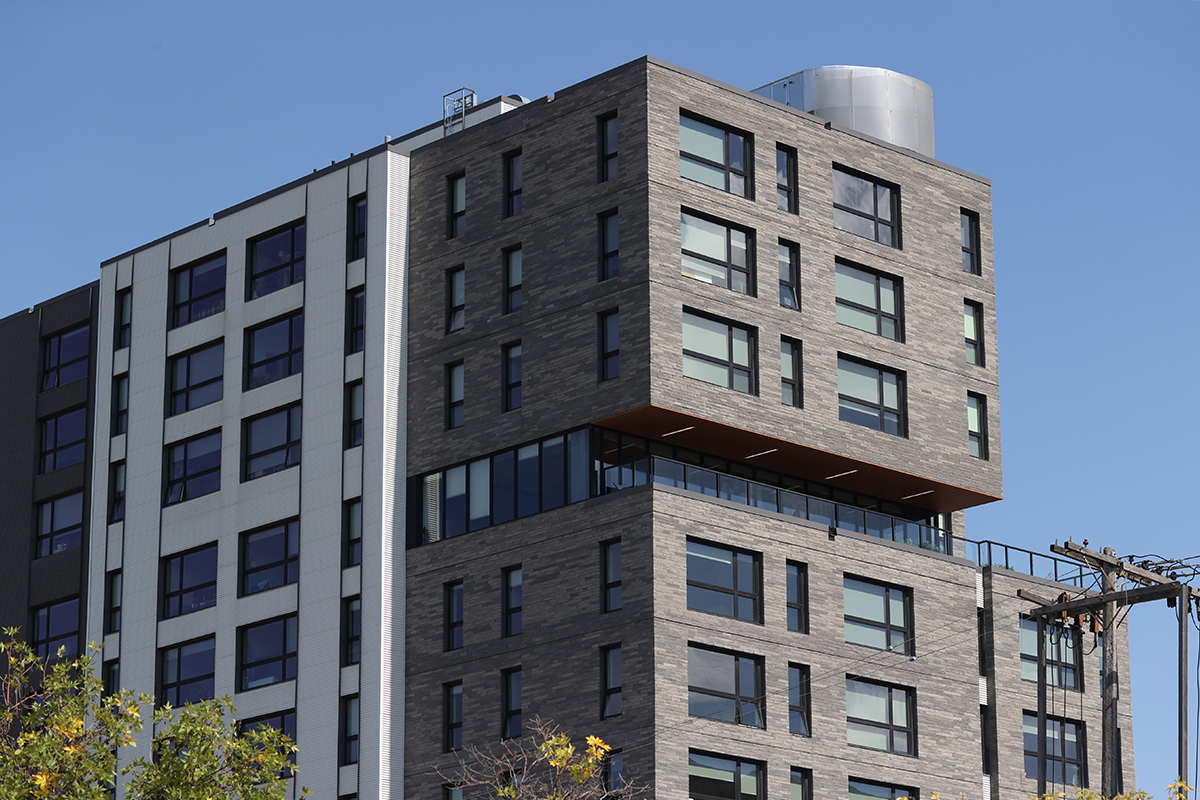 The tall, grey, residential West Broadway Commons building in Winnipeg in a sunny day.