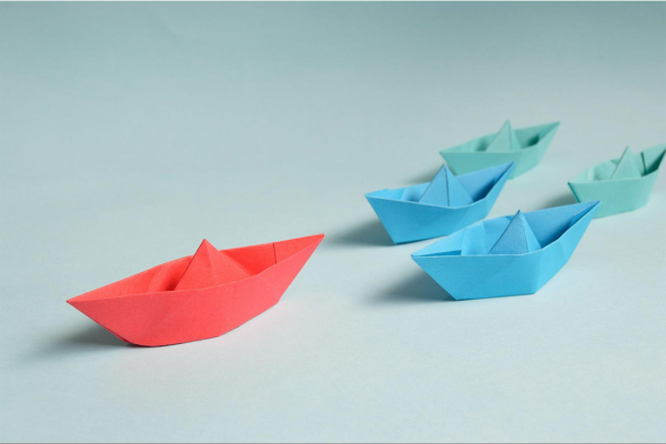 3 paper boats. One red ahead of 2 blue boats.