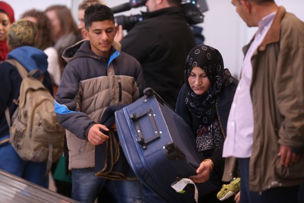 A woman wearing a headscarf removes a blue bag from a luggage conveyor at Winnipeg's international airport as a boy looks on.