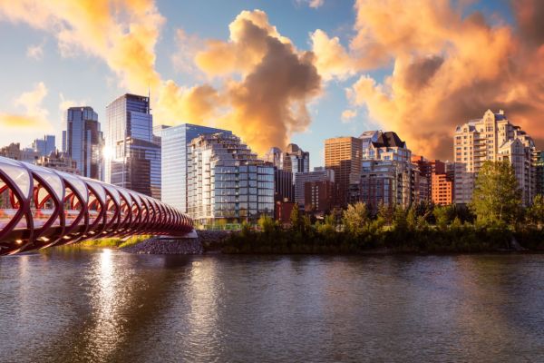 Peace Bridge across Bow River with Modern City Buildings in Background during a vibrant summer sunrise. Cloudy Sky Composite. Taken in Calgary, Alberta, Canada.